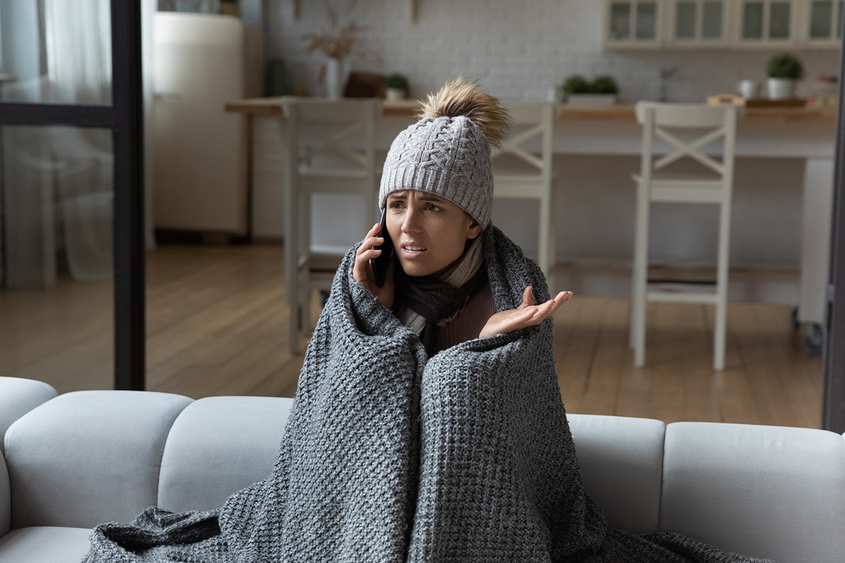 Woman wrapped in blanket making phone call, cold at home